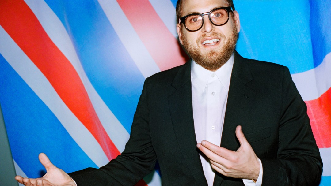 Jonah Hill en traje con fondo azul y rojo